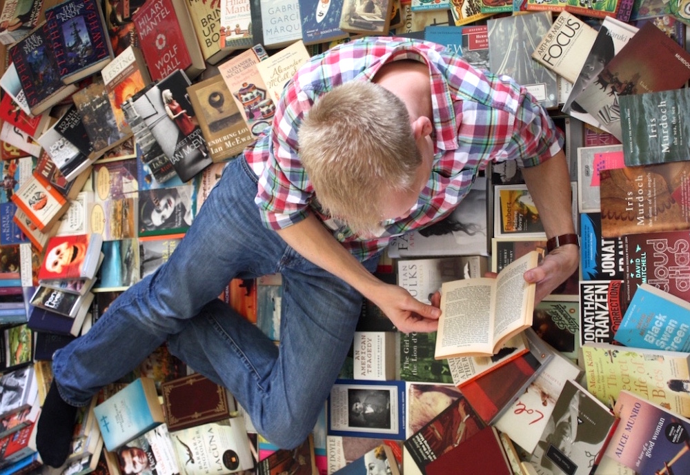 Photo of me reading, lying on a mass of books