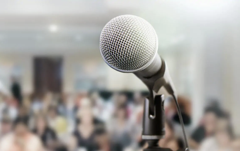 Photo of a microphone with auditorium in the background